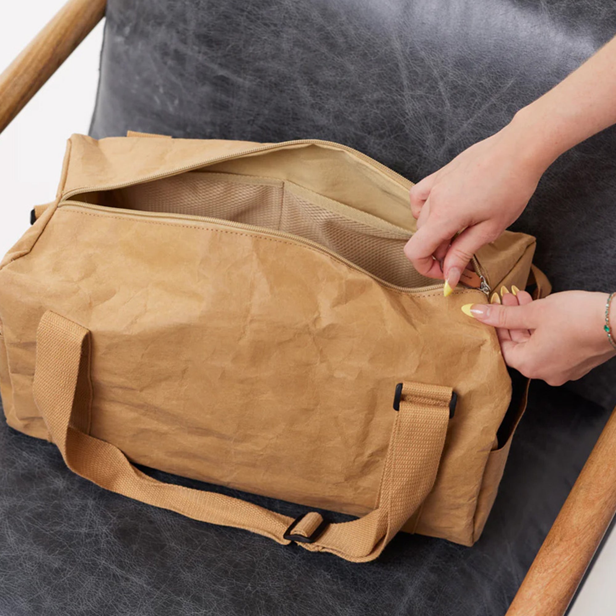 Jakob Kraft Paper Duffle Bag sitting on a chair while someone zips it up, highlighting its stylish and eco-friendly design with practical zipper functionality.